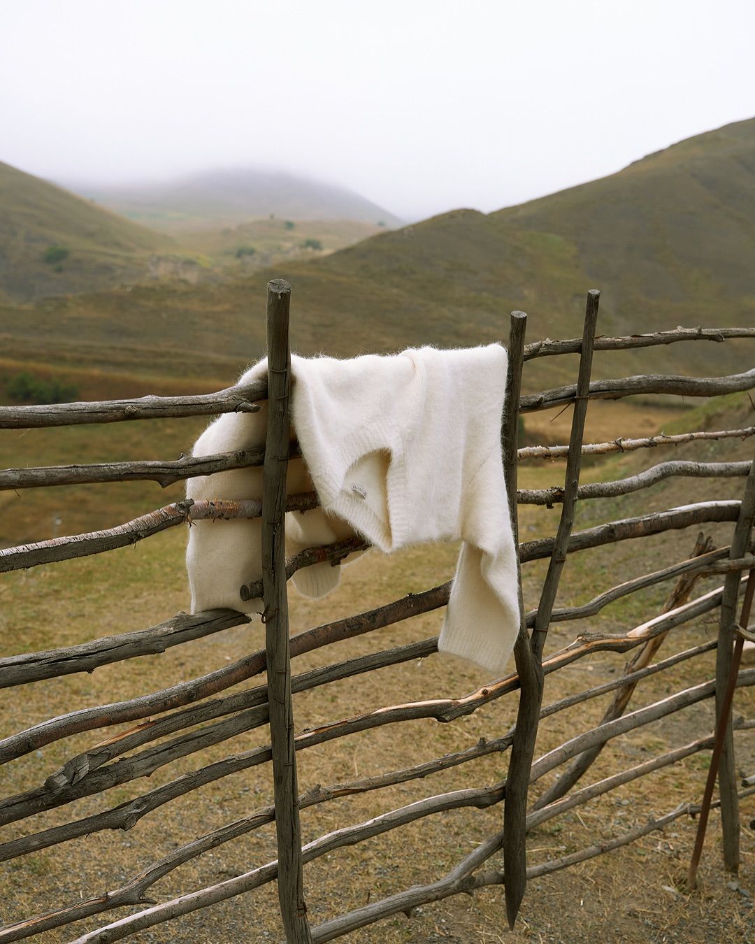 A cream jumper hanging on a wooden fence in the hills